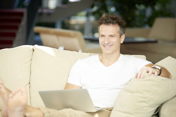 Portrait of a casual man working on his laptop at home while sitting on couch at living room.