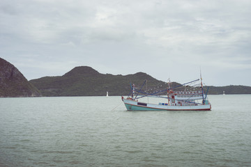 traditional fishing boat laying on the sea with big and long mountain in background.cloudy sky.filtered image.selective focus
