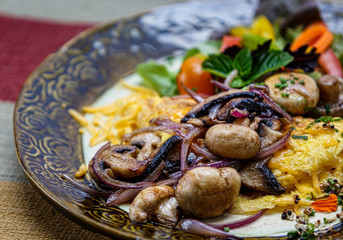Omelette with mixed vegetables and cheese, the different vegetables are mushroom, onion, carrots, tomatoe, green leaf salad and mint leaves. In a beautifully decorated plate on a table cloth.