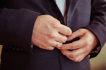 Closeup of married man's hands buttoning up black jacket