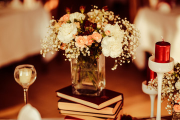 Glass vase with tiny daisies and white roses stands on the books