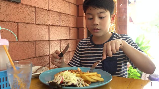 Little asian child eating pork steak at restaurant ,happy asian boy enjoy at your meal.