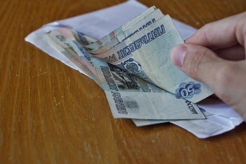 Male hand opening a white envelope full of Russian currency (Russian Ruble, RUB) on the wooden table as a symbol of cash transfer, money laundering or bribery
in Russia