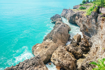 Scenic view from high mountain cliff on colorful blue Indian ocean water hitting rocks in Bali, Indonesia. Sea nature landscape