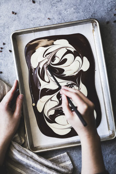Person drawing in melted white and dark chocolate