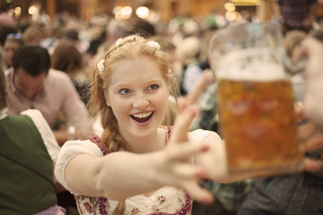 Excited girl reaches for a mug of beer at Oktoberfest