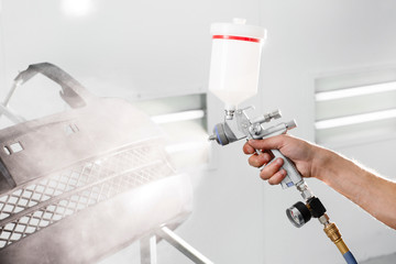 worker painting a car black blank parts in special garage, wearing costume and protective gear