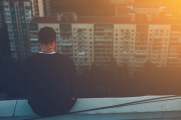 Fototapeta premium Brave man sitting and chilling on the edge of the roof at sunset