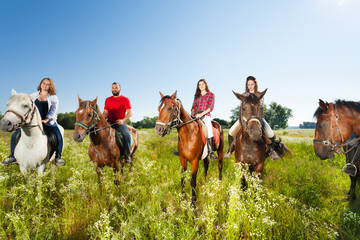 Naklejka premium Happy equestrians riding horses in summer field