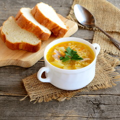 Chicken soup with noodles, potatoes, onions and carrots. Chicken soup in a bowl, sliced bread, spoon on old wooden table. Rustic style. Closeup