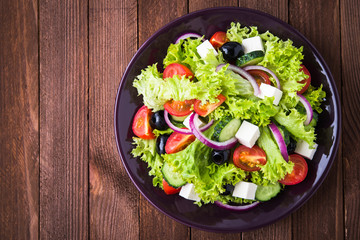 Greek salad (lettuce, tomatoes, feta cheese, cucumbers, black olives, purple onion) on dark wooden...