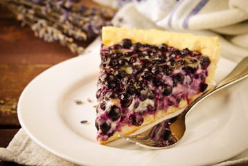 Bilberry, blueberry tart with lavender on white plate, wooden background