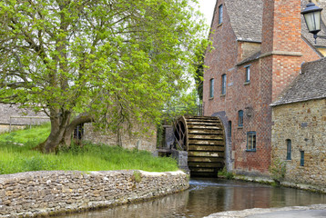 Old water mill with undershot waterwheel  and red brick chimney on the edge of traditional english village © Yols