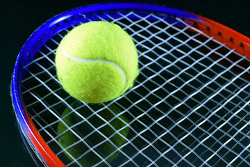 Tennis racket with a tennis ball closeup on black background.