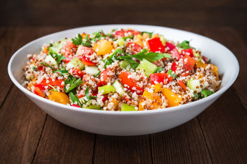 Fresh healthy salad with quinoa, colorful tomatoes, sweet pepper, cucumber and parsley on wooden background close up. Food and health. Superfood meal.
