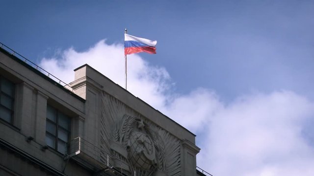 Russian Administrative Concrete Building. Soviet Union Symbols in Front. Russian Federation Tricolor on Top. Facade Decorated With Old Coat of Arms