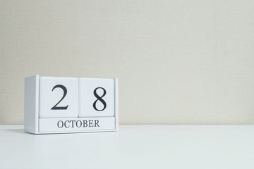 Closeup white wooden calendar with black 28 october word on blurred white wood desk and cream color wallpaper in room textured background with copy space , selective focus at the calendar