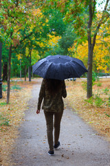 Young girl walking on a path in a forest a rainy day. She goes with an umbrella against the rain. The forest is very colorful. 