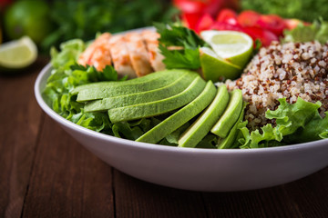 Healthy salad bowl with quinoa, tomatoes, chicken, avocado, lime and mixed greens (lettuce, parsley) on wooden background close up. Food and health.