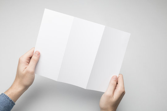 Hands Are Holding A Dl Tri-Fold White Paper Flyer