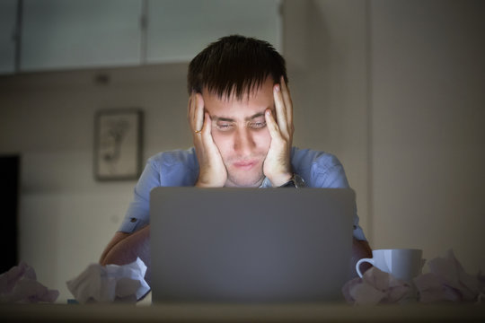 Portrait of a man grabbing his head in despair at the desk near the laptop, late at night. Education, business concept photo. Lifestyle