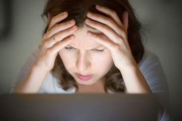 Portrait of a woman grabbing her head at the desk near the laptop, late at night. Education, business concept photo. Lifestyle, closeup