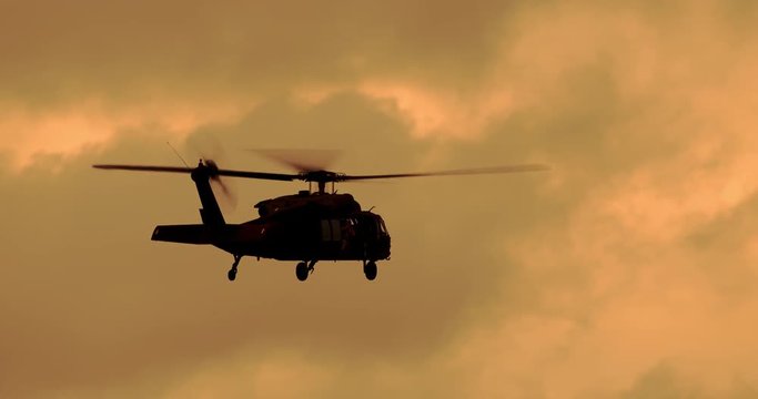 Tracking shot of black hawk helicopter flying in sky during sunset