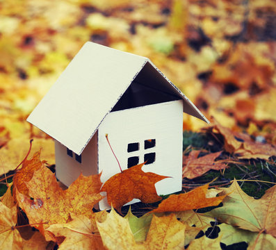 House from paper in bright yellow autumn leaves. Model of cardboard house. Concept image house. Concept of sale or purchase house