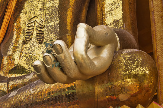 Golden Buddha hand on knee of statue closeup