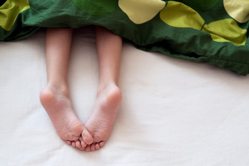 Child's feet under blanket - obrazy, fototapety, plakaty