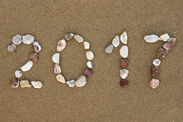 Fototapeta na wymiar Pebble made New Year 2017 number on wet sandy beach 