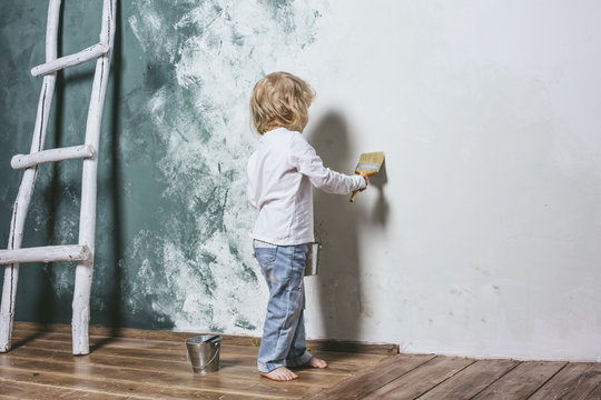 Little beautiful and happy child in jeans paint the wall with br