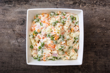 Russian salad in white bowl on rustic wooden

