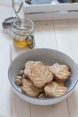 Maple leaf shaped cookies in a white bowl. Maple syrup in a glass jar in the background 