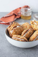 Carrot cake cookies  with creamy filling . Gray tabletop, maple syrup in a jar and an orange towel in the background. 