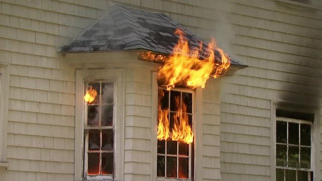 House window burning in fire as flames shoot out of the window and burn the wall