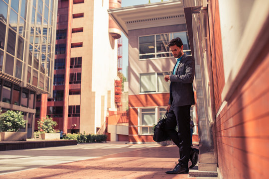 Elegant businessman looking at watch in the street