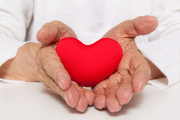 Old hands of the elderly giving a red heart