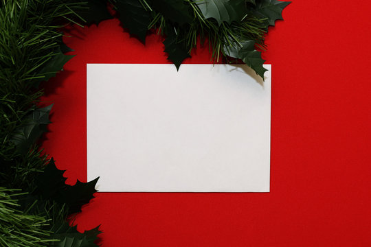 White sheet of paper in a frame of branches of Christmas tree and red balls on a red background