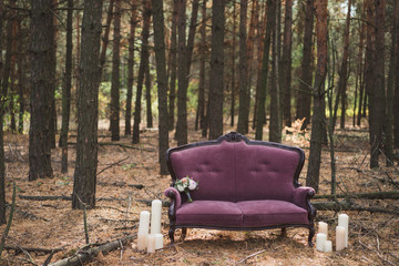 purple sofa with candles around it and a bouquet on it stand in the forest