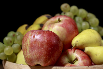 Red apple in front of heap of different fruits, on black