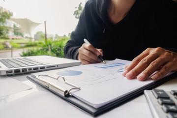 Asian business woman manager analyzing datum in charts and typing on computer, making notes in documents on the table in office, vintage color, selective focus. Business concept...