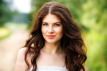 Beautiful young woman close-up in white dress, against green of  park.