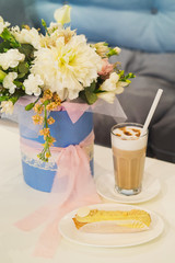 Latte in a glass and fresh eclair on dessert dish, bouquet of flowers on the background. Blank...