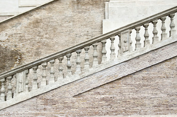 White stone staircase with columns under the railing. The staircase is on the wall of the small light brick.
