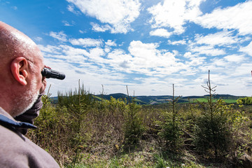 man looking with binoculars to panoramic view of low mountain range, germany