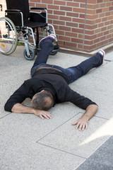 man lying on pavement next to wheelchair