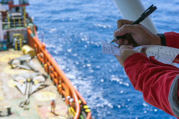 Offshore worker taking note while performing anchor handling operation at Terengganu oilfield,...