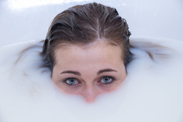 Portrait photo of a blonde girl with blue eyes bathing in a bathtub full of water and milk. 