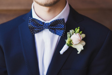 closeup of groom's boutonniere, dotted bow tie, white shirt and blue jacket